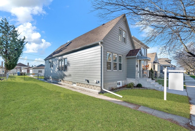 view of home's exterior featuring a residential view, a lawn, a shingled roof, and fence