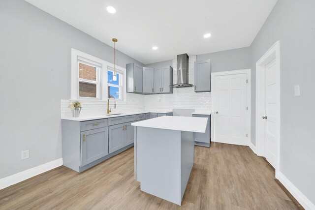 kitchen with a sink, wall chimney exhaust hood, gray cabinetry, and decorative backsplash