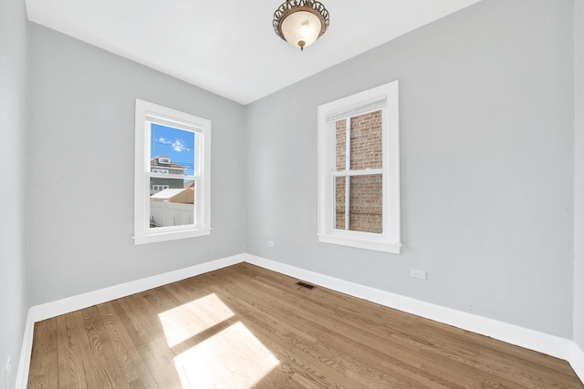 empty room featuring wood finished floors, visible vents, and baseboards