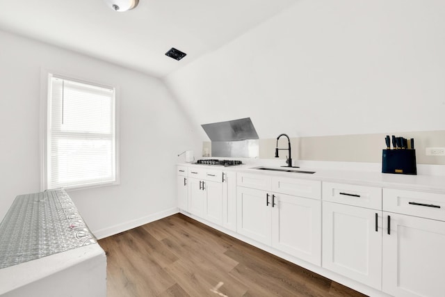 bar with stainless steel gas cooktop, vaulted ceiling, a sink, baseboards, and light wood-type flooring