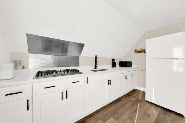 kitchen featuring stainless steel gas stovetop, freestanding refrigerator, light wood-style floors, a sink, and wall chimney exhaust hood