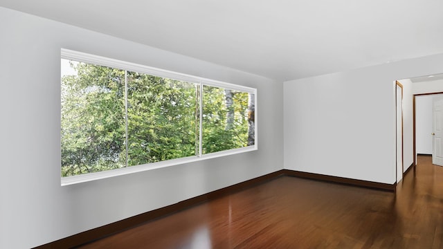 empty room with a healthy amount of sunlight, dark wood finished floors, and baseboards
