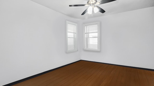 spare room featuring dark wood-type flooring, a ceiling fan, and baseboards