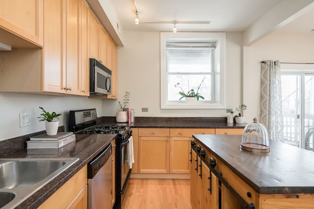 kitchen with track lighting, appliances with stainless steel finishes, a kitchen island, and light wood finished floors