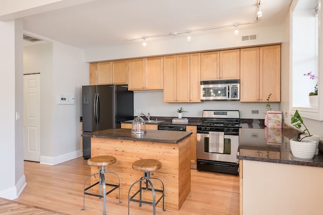 kitchen with light brown cabinets, a kitchen breakfast bar, light wood-style flooring, stainless steel appliances, and visible vents