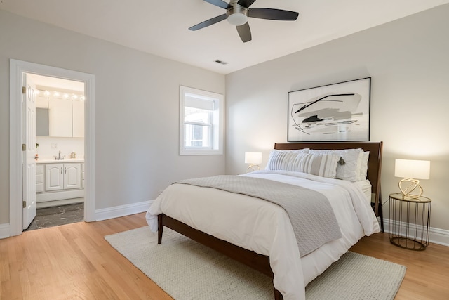 bedroom featuring visible vents, baseboards, light wood-type flooring, a sink, and ensuite bath