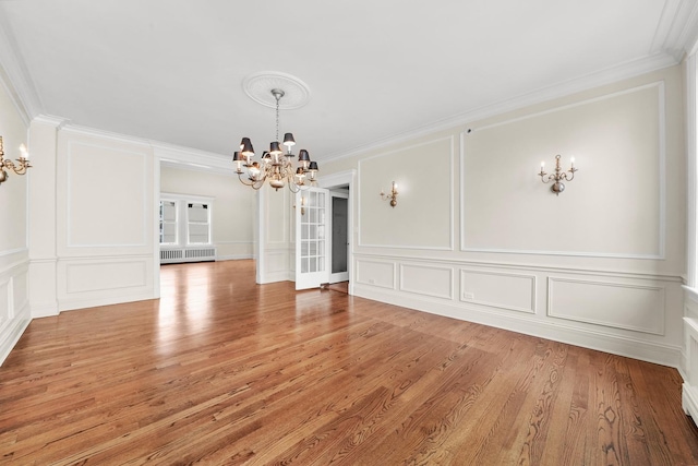 unfurnished dining area featuring radiator, crown molding, a chandelier, and a decorative wall