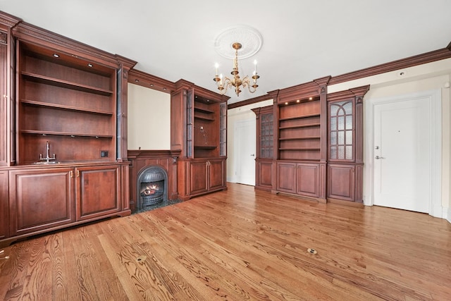 unfurnished living room featuring light wood finished floors, a sink, a notable chandelier, a lit fireplace, and crown molding