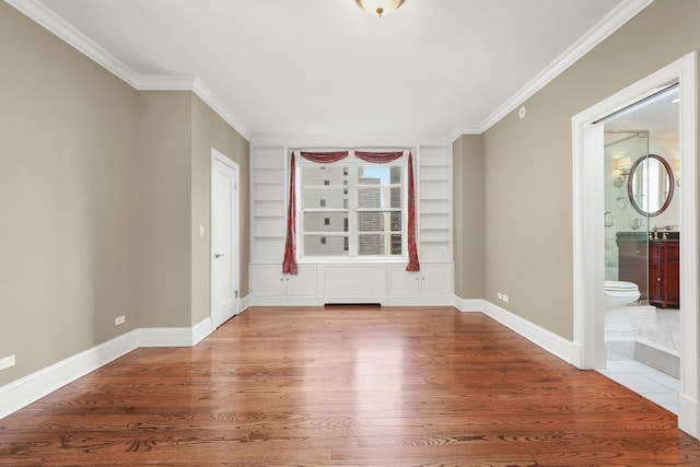 unfurnished room featuring built in shelves, crown molding, wood finished floors, and baseboards