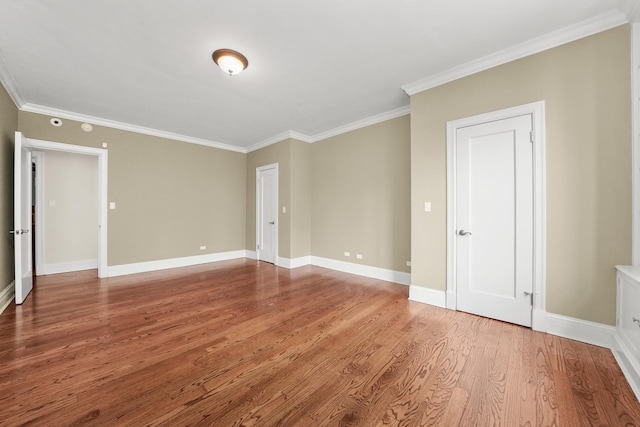 spare room with wood finished floors, crown molding, and baseboards