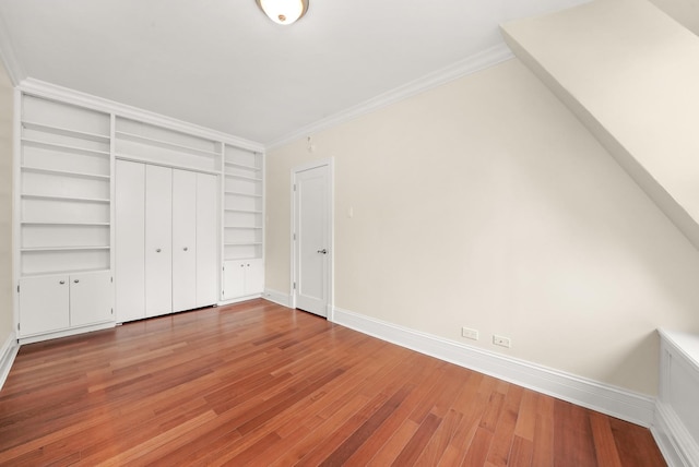 unfurnished bedroom featuring light wood-style floors, a closet, crown molding, and baseboards