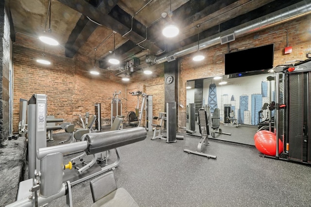 gym featuring a towering ceiling, visible vents, and brick wall