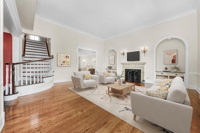 living area featuring baseboards, ornamental molding, a fireplace, wood finished floors, and stairs