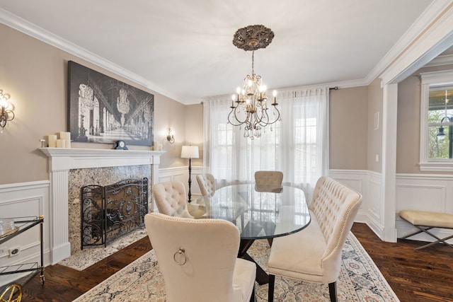 dining space with a chandelier, dark wood finished floors, ornamental molding, a decorative wall, and a wainscoted wall