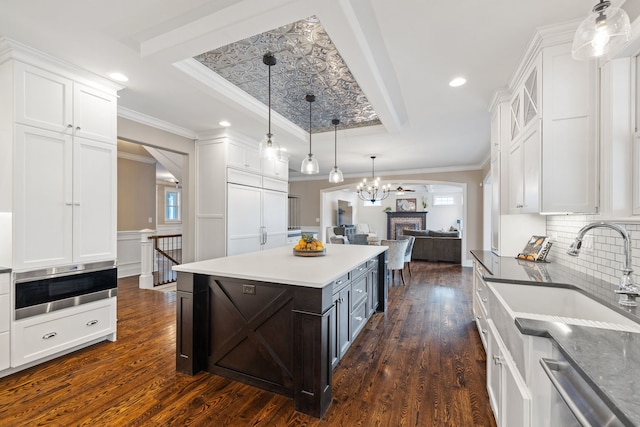 kitchen with a raised ceiling, a sink, white cabinetry, dark wood-style floors, and healthy amount of natural light