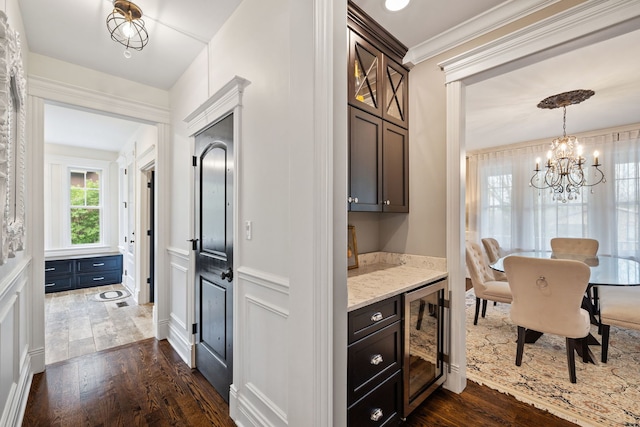 kitchen featuring beverage cooler, dark wood-type flooring, a chandelier, light stone countertops, and crown molding