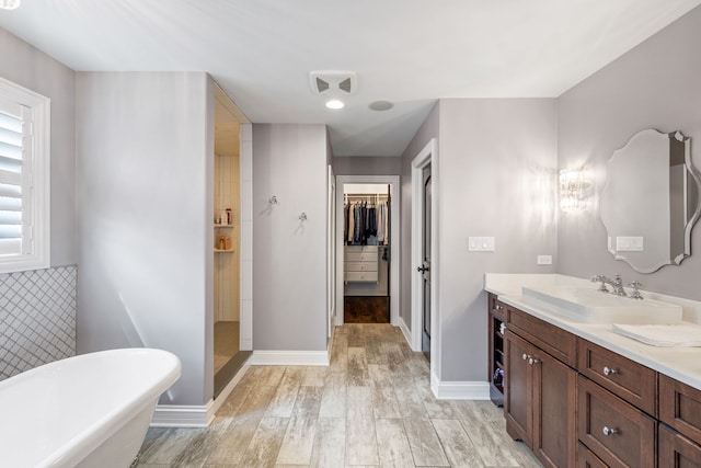 full bath with vanity, a freestanding tub, tiled shower, a walk in closet, and wood finished floors