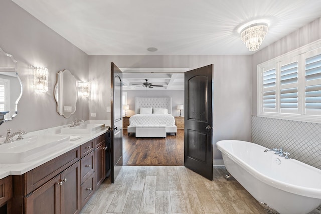 ensuite bathroom with wood finished floors, a soaking tub, a ceiling fan, double vanity, and beam ceiling