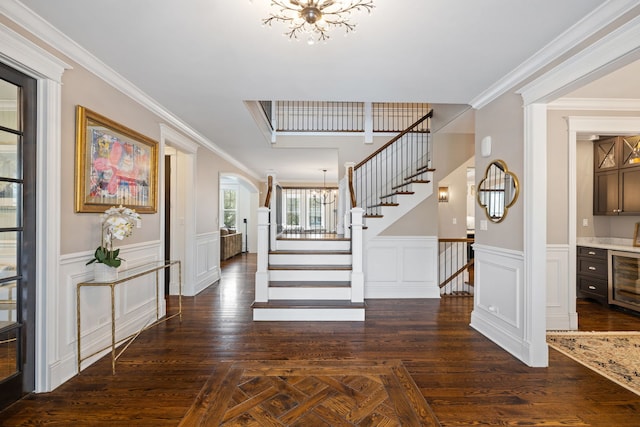 foyer featuring a chandelier, stairs, wine cooler, a wainscoted wall, and arched walkways