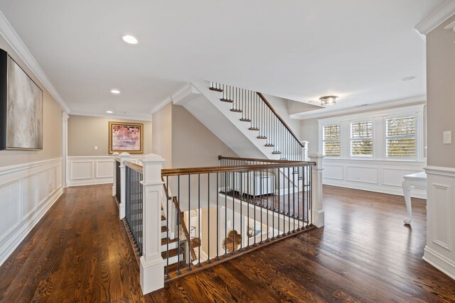 corridor with a decorative wall, ornamental molding, dark wood-style flooring, an upstairs landing, and a wainscoted wall