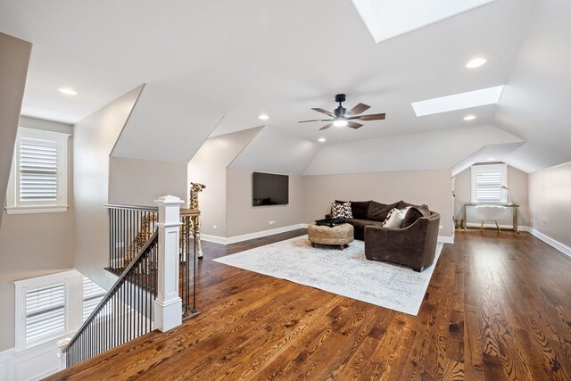 living area featuring a skylight, lofted ceiling, ceiling fan, dark wood finished floors, and baseboards