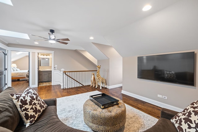 living room with a ceiling fan, a skylight, wood finished floors, baseboards, and vaulted ceiling