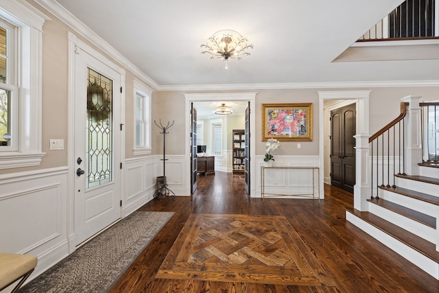 entrance foyer with stairs, a decorative wall, ornamental molding, dark wood-type flooring, and a wainscoted wall