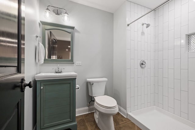 full bath with toilet, tiled shower, vanity, and baseboards
