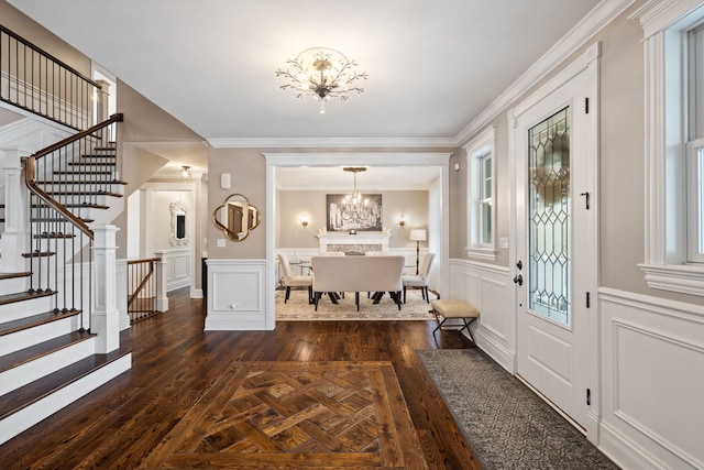 entrance foyer with a chandelier, a decorative wall, stairs, a wainscoted wall, and crown molding