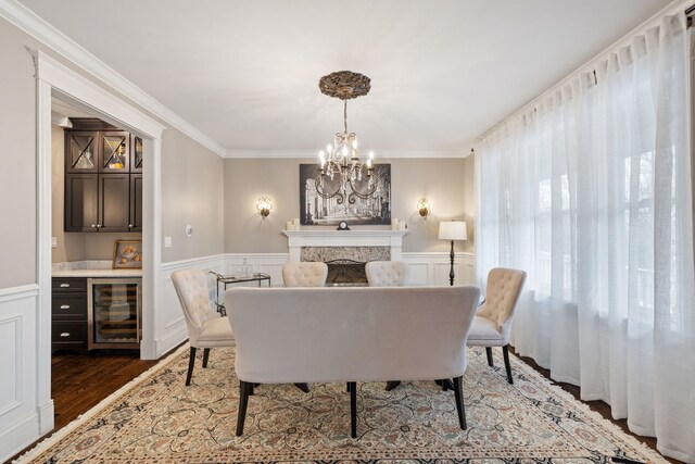 dining space featuring wine cooler, a chandelier, wood finished floors, a wainscoted wall, and ornamental molding