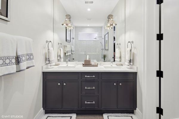 full bath featuring a tile shower, double vanity, a sink, baseboards, and visible vents