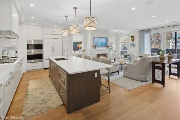 kitchen with an island with sink, stainless steel appliances, white cabinets, a kitchen bar, and a sink