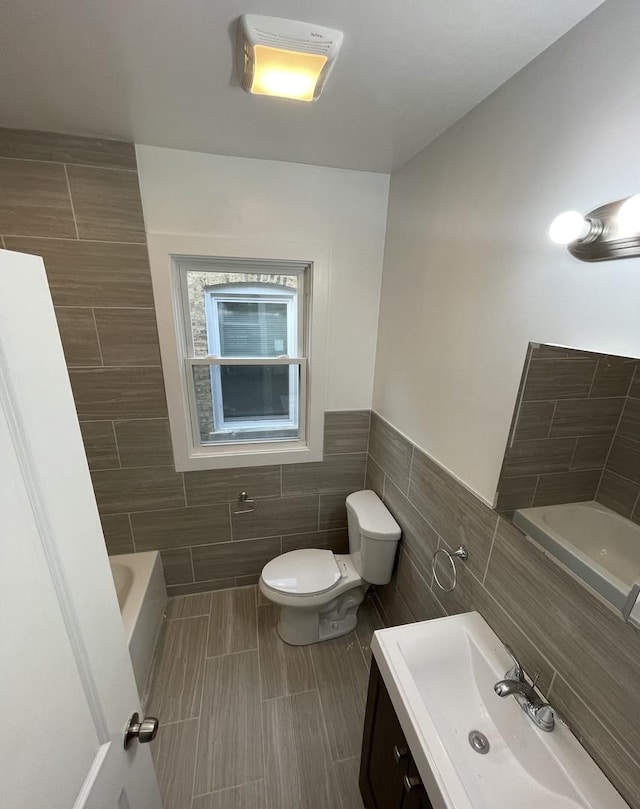 bathroom with toilet, a wainscoted wall, a bathtub, tile walls, and vanity