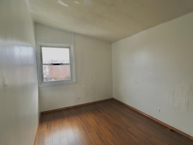 spare room with baseboards, wood finished floors, and vaulted ceiling
