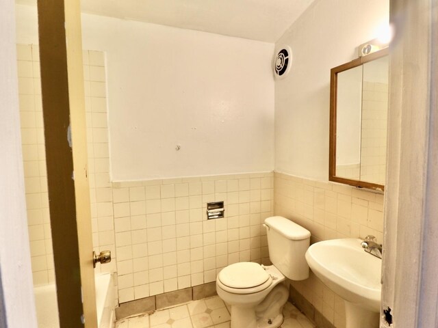 full bathroom with tile walls, a sink, a bathtub, toilet, and wainscoting