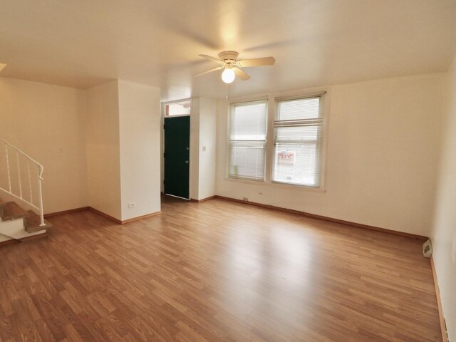unfurnished living room featuring baseboards, wood finished floors, a ceiling fan, and stairs