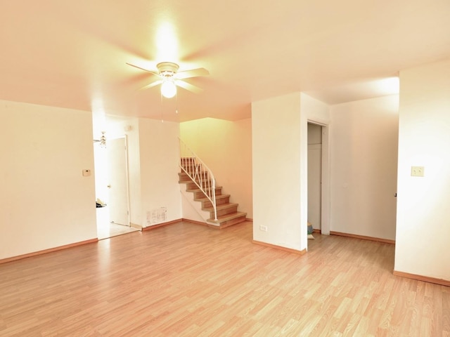 unfurnished living room featuring baseboards, a ceiling fan, stairway, and light wood-style floors