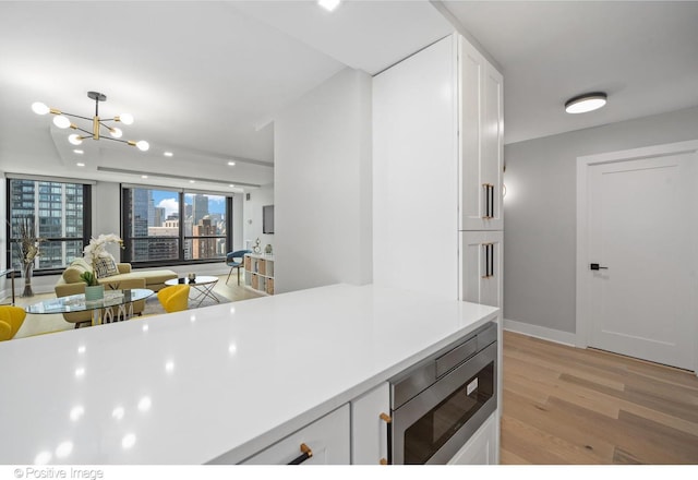 1030 N State St Unit 21K, Chicago, IL 60610 - kitchen featuring stainless steel microwave, white cabinetry, light countertops, an inviting chandelier, and light wood-type flooring