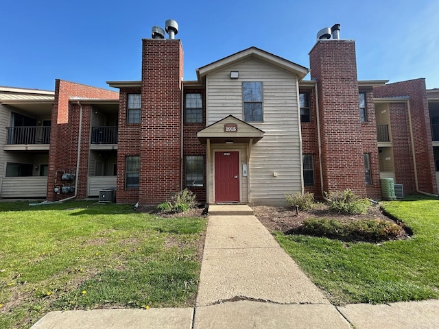 1915 N Hicks Rd Unit 105, Palatine, IL 60074 - view of front of property featuring a front yard, central air condition unit, brick siding, and a chimney