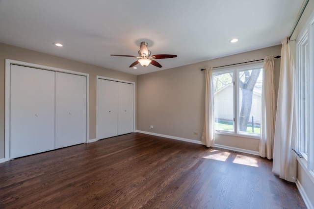 unfurnished bedroom featuring baseboards, multiple closets, dark wood-style flooring, and visible vents