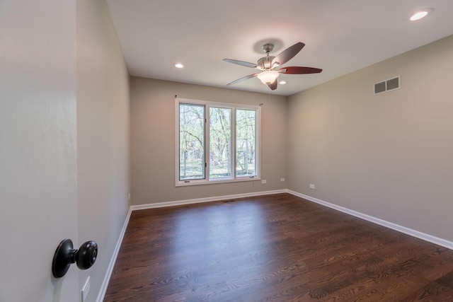 empty room featuring dark wood-style flooring, a ceiling fan, baseboards, and visible vents