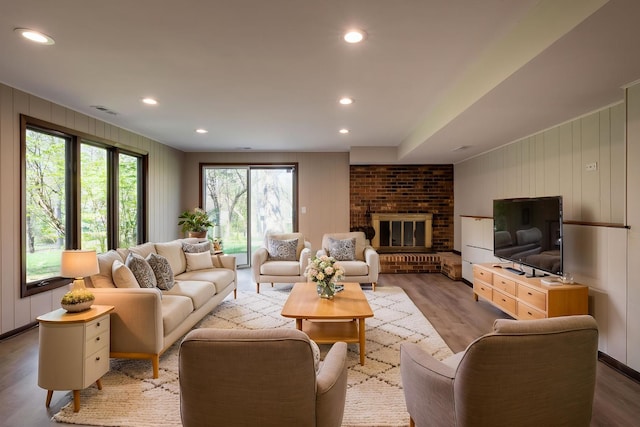 living room featuring a brick fireplace, recessed lighting, wood finished floors, and visible vents