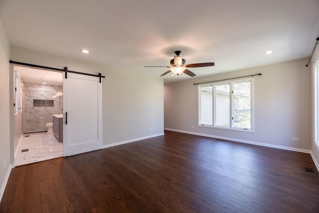 empty room with baseboards, a barn door, dark wood-style flooring, and ceiling fan