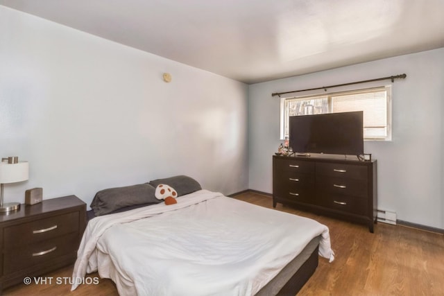 bedroom featuring baseboards, wood finished floors, and a baseboard radiator