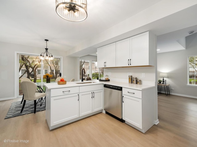 kitchen featuring stainless steel dishwasher, light wood-style flooring, a sink, an inviting chandelier, and a peninsula