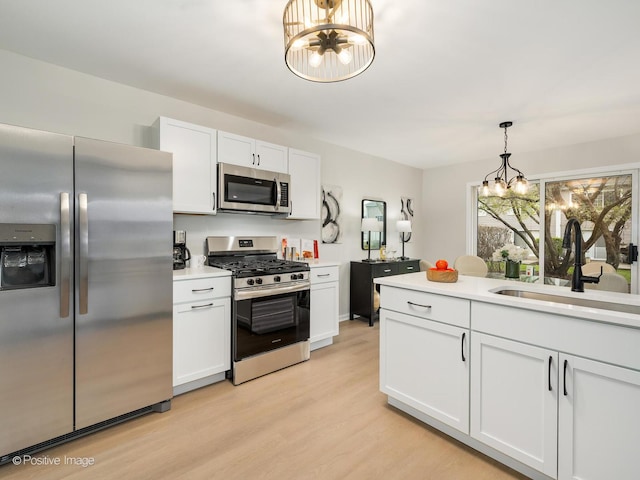 kitchen with a sink, appliances with stainless steel finishes, light countertops, light wood finished floors, and a notable chandelier