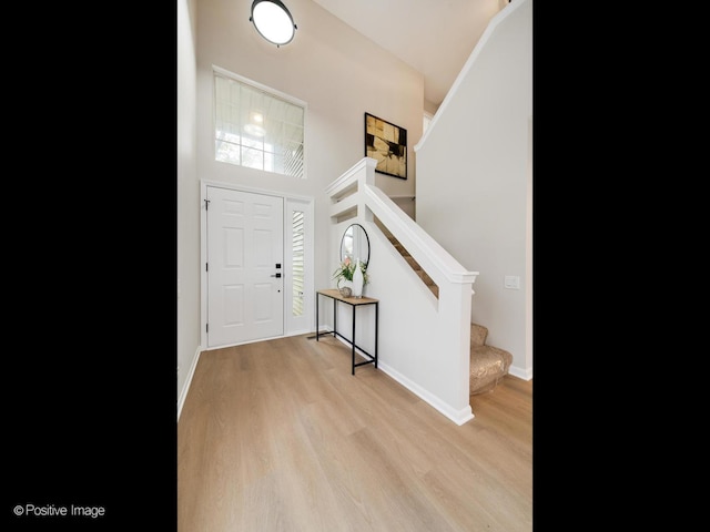 foyer entrance with stairway, light wood-type flooring, baseboards, and a high ceiling