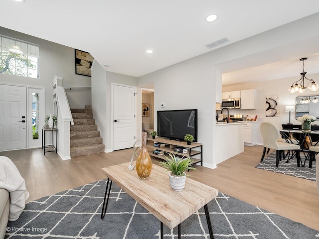 living area featuring light wood finished floors, recessed lighting, an inviting chandelier, stairs, and visible vents