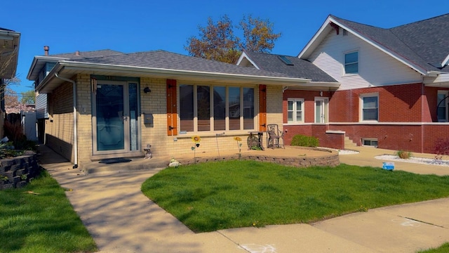 view of front of house with brick siding, a shingled roof, and a front yard