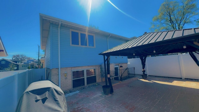 exterior space featuring a fenced backyard, a standing seam roof, a gazebo, brick siding, and metal roof
